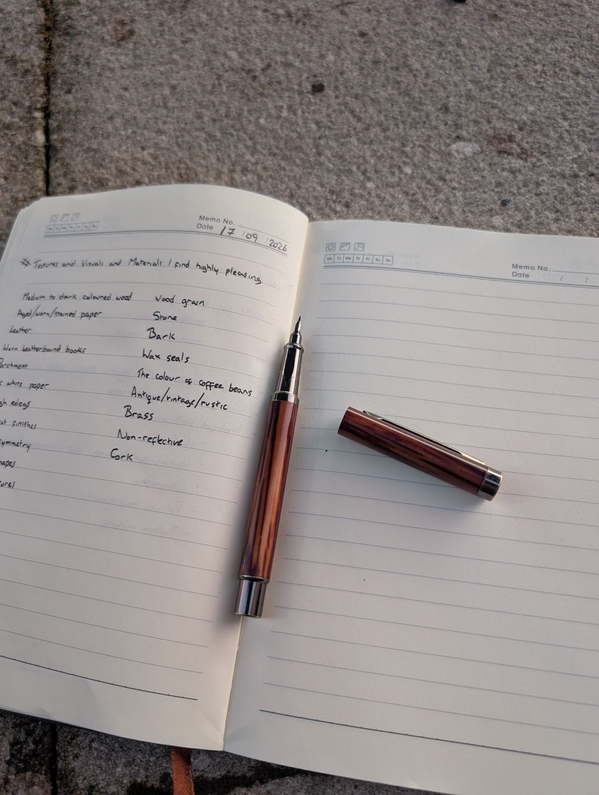 A wooden fountain pen resting on an open notebook, outside on paving stones